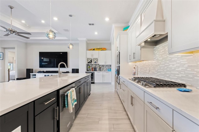 kitchen with custom range hood, white cabinetry, pendant lighting, and sink