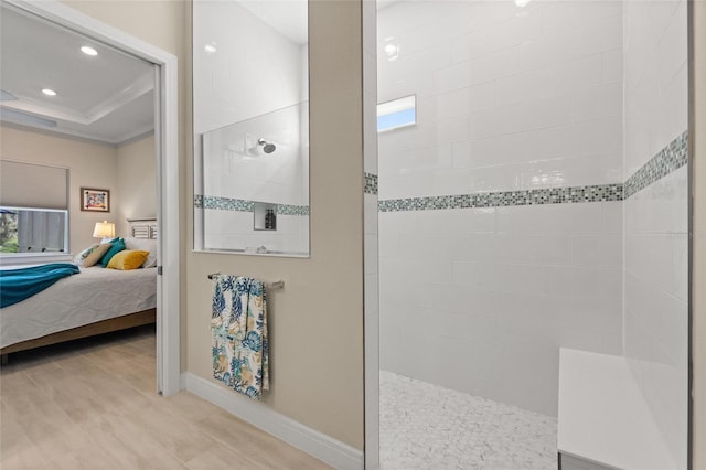 bathroom with a tile shower, a tray ceiling, ornamental molding, and wood-type flooring