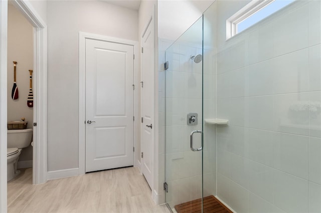 bathroom featuring hardwood / wood-style floors, a shower with shower door, and toilet