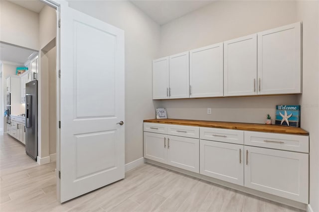 kitchen with white cabinets, light hardwood / wood-style floors, stainless steel refrigerator with ice dispenser, and wood counters