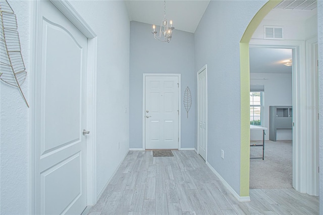 hall with light hardwood / wood-style floors, lofted ceiling, and an inviting chandelier