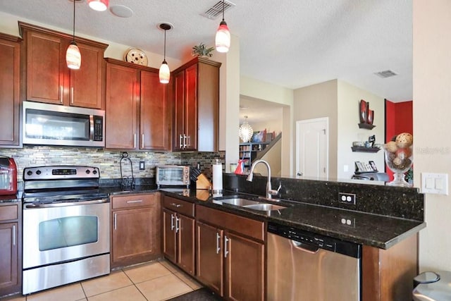 kitchen with sink, hanging light fixtures, stainless steel appliances, dark stone countertops, and a textured ceiling