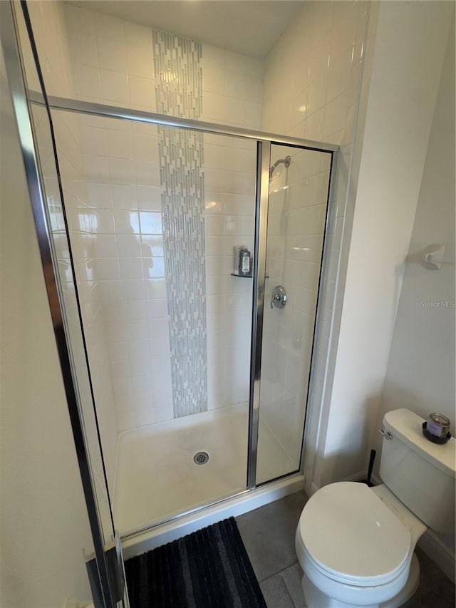 bathroom with tile patterned floors, toilet, and a shower with door