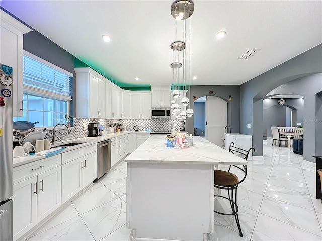 kitchen with pendant lighting, backsplash, white cabinets, a kitchen island, and stainless steel appliances