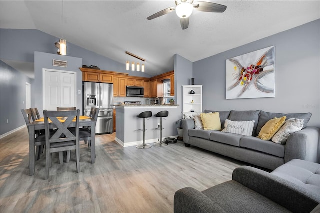 living room featuring a textured ceiling, ceiling fan, vaulted ceiling, and light wood-type flooring