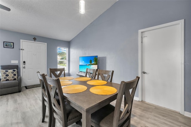 dining space featuring a textured ceiling, light hardwood / wood-style flooring, and vaulted ceiling