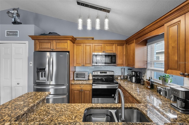 kitchen with pendant lighting, stainless steel appliances, lofted ceiling, and dark stone countertops