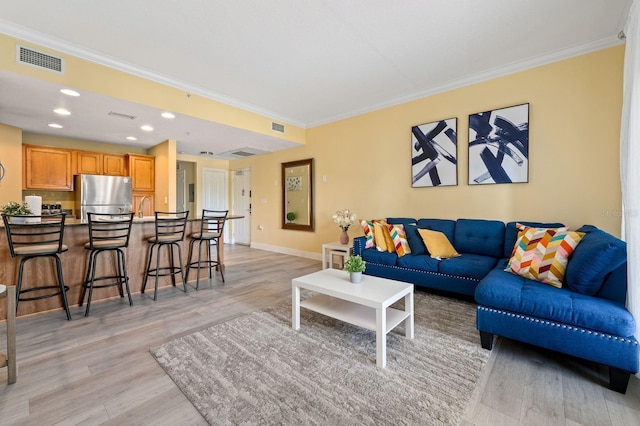 living room with sink, light wood-type flooring, and ornamental molding