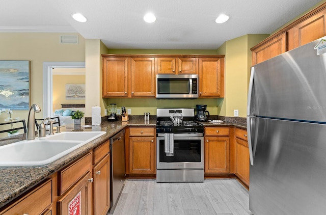 kitchen with light hardwood / wood-style floors, dark stone countertops, sink, and appliances with stainless steel finishes