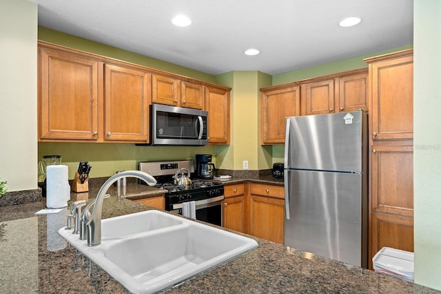 kitchen featuring appliances with stainless steel finishes, dark stone countertops, and sink