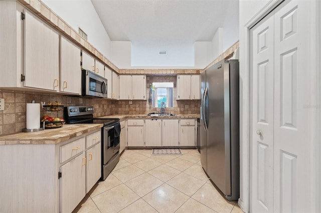 kitchen featuring decorative backsplash, a textured ceiling, stainless steel appliances, sink, and light tile patterned floors