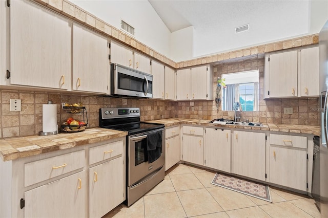 kitchen featuring appliances with stainless steel finishes, light tile patterned floors, tile counters, and lofted ceiling