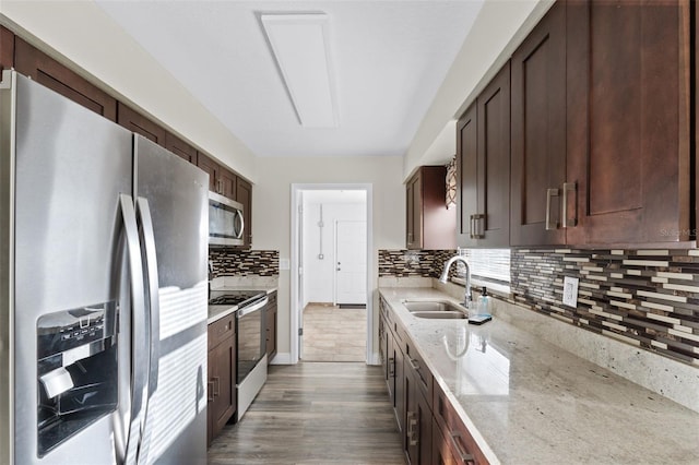 kitchen featuring appliances with stainless steel finishes, tasteful backsplash, light stone counters, sink, and wood-type flooring