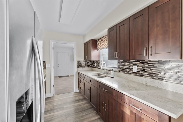 kitchen with light stone countertops, sink, tasteful backsplash, stainless steel refrigerator with ice dispenser, and light hardwood / wood-style floors