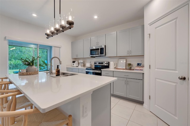 kitchen featuring a center island with sink, gray cabinets, sink, and appliances with stainless steel finishes