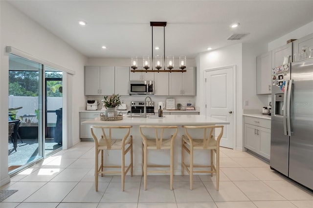 kitchen with sink, stainless steel appliances, an island with sink, a chandelier, and pendant lighting