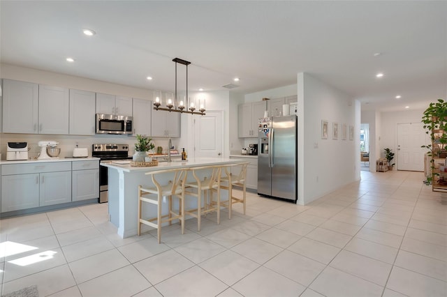 kitchen featuring an island with sink, decorative light fixtures, gray cabinets, light tile patterned floors, and appliances with stainless steel finishes