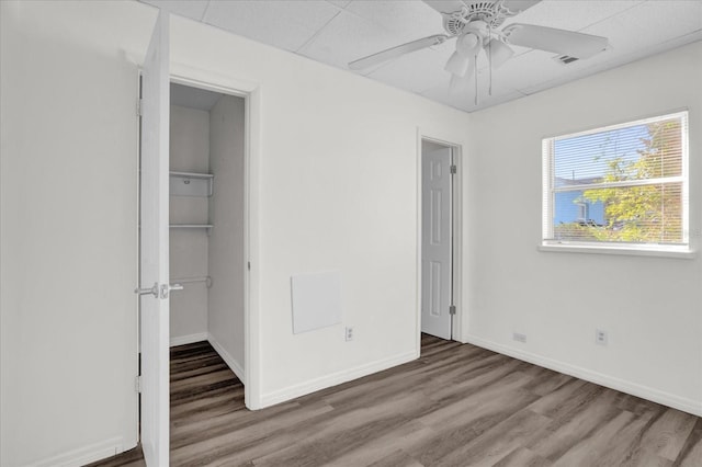 unfurnished bedroom featuring ceiling fan, a walk in closet, wood-type flooring, and a closet