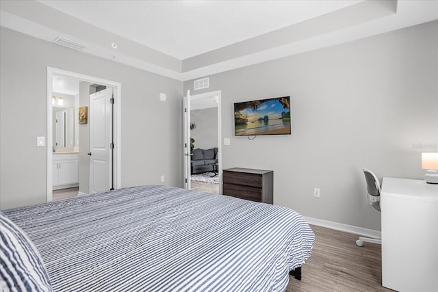 bedroom with ensuite bathroom, light wood-type flooring, and a tray ceiling