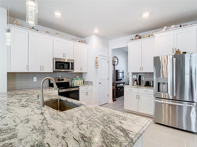 kitchen with white cabinetry, sink, light stone countertops, stainless steel appliances, and backsplash