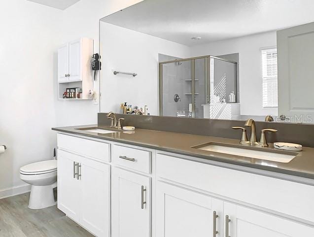 bathroom with wood-type flooring, vanity, toilet, and a shower with shower door