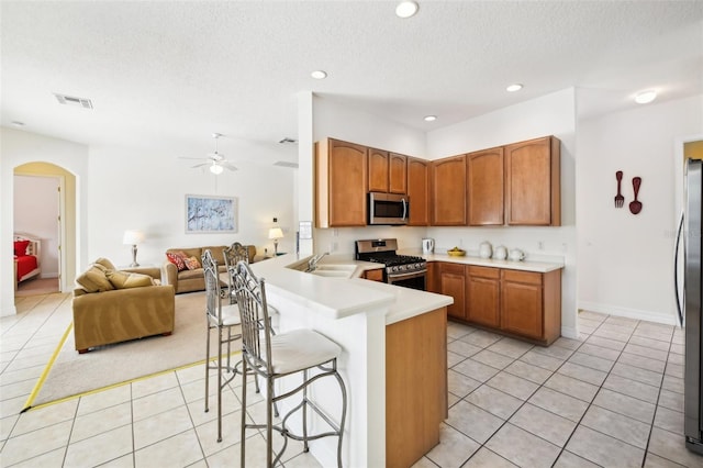 kitchen with kitchen peninsula, appliances with stainless steel finishes, a kitchen bar, a textured ceiling, and sink