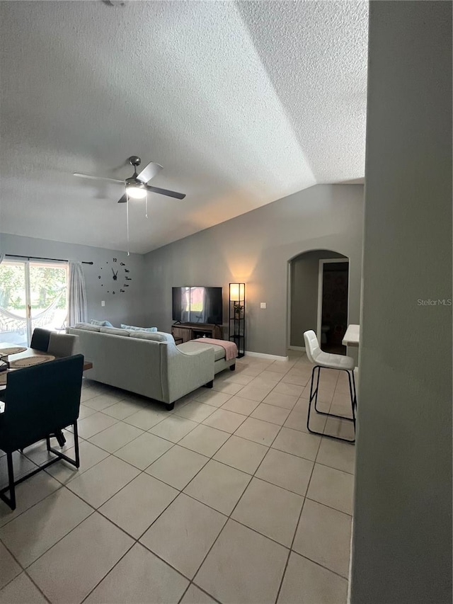 living room featuring vaulted ceiling, ceiling fan, light tile patterned flooring, and a textured ceiling