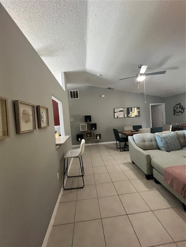 living room featuring light tile patterned floors, a textured ceiling, vaulted ceiling, and ceiling fan