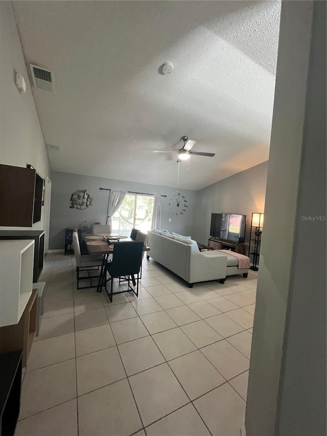 living room with ceiling fan, light tile patterned floors, a textured ceiling, and vaulted ceiling