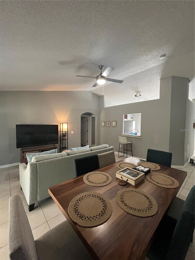 tiled dining room featuring ceiling fan, lofted ceiling, and a textured ceiling