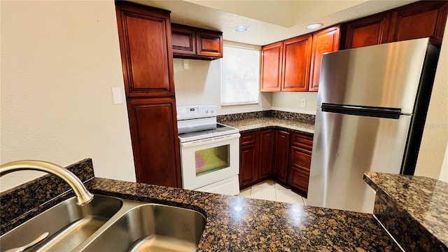 kitchen featuring stainless steel fridge, dark stone counters, sink, light tile patterned floors, and white electric stove