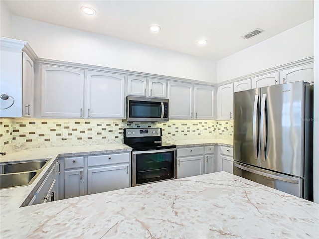 kitchen with gray cabinetry, sink, stainless steel appliances, tasteful backsplash, and light stone counters