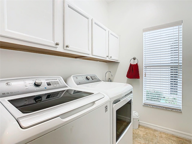 laundry room with light tile patterned floors, cabinets, separate washer and dryer, and a wealth of natural light