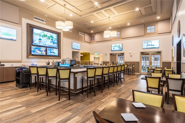 bar featuring pendant lighting, an inviting chandelier, a raised ceiling, light wood-type flooring, and a towering ceiling