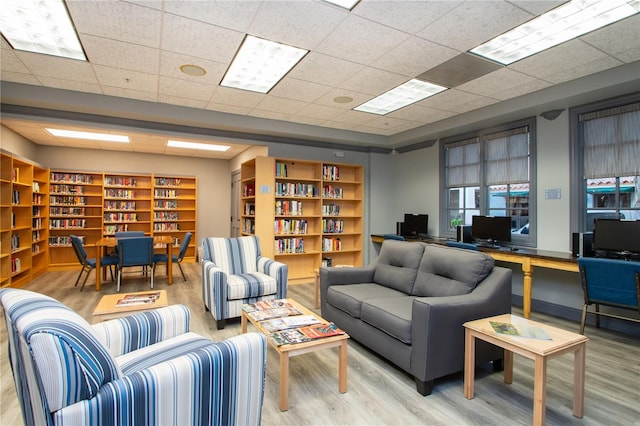 living room with a drop ceiling, light hardwood / wood-style floors, and built in features