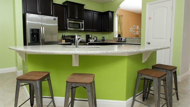 kitchen with a kitchen bar, light stone countertops, a kitchen island with sink, and appliances with stainless steel finishes