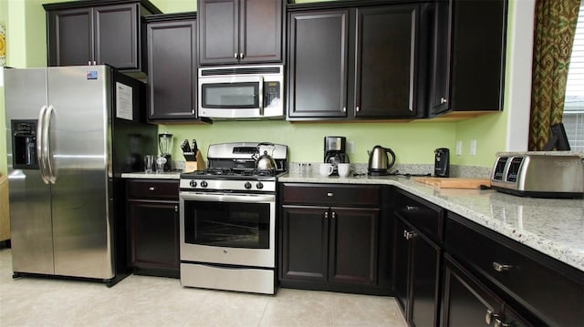 kitchen featuring light stone counters, dark brown cabinetry, stainless steel appliances, and light tile patterned floors