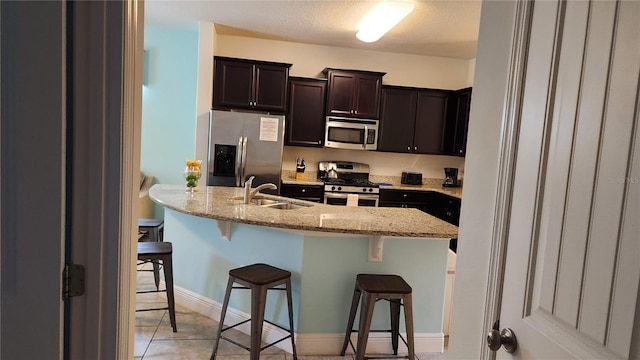 kitchen featuring sink, a kitchen breakfast bar, light stone counters, light tile patterned floors, and appliances with stainless steel finishes