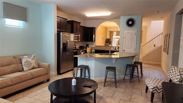 kitchen featuring light stone countertops, sink, an inviting chandelier, a breakfast bar, and appliances with stainless steel finishes