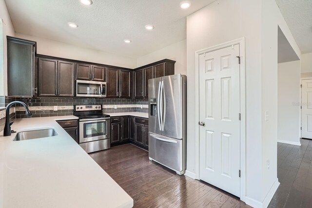 kitchen featuring sink, dark hardwood / wood-style floors, a textured ceiling, decorative backsplash, and appliances with stainless steel finishes