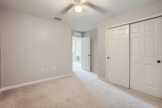 unfurnished bedroom featuring ceiling fan, a closet, light colored carpet, and a textured ceiling