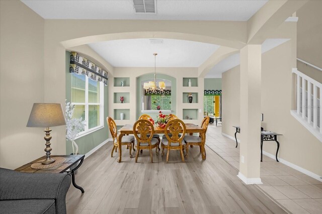 dining room with an inviting chandelier, built in features, and light hardwood / wood-style flooring