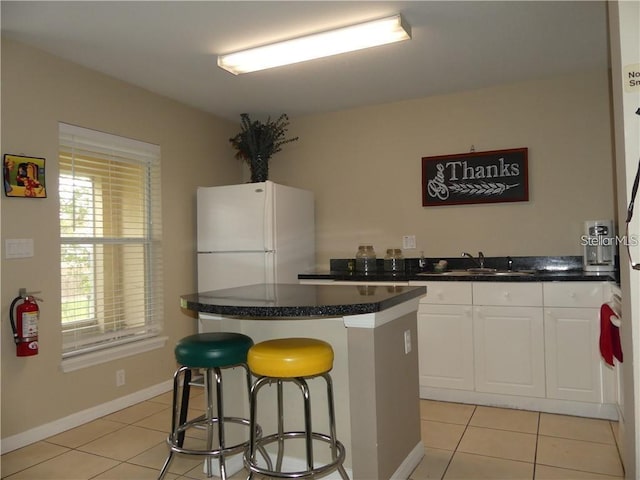 kitchen featuring white cabinetry, a center island, sink, white refrigerator, and a kitchen bar