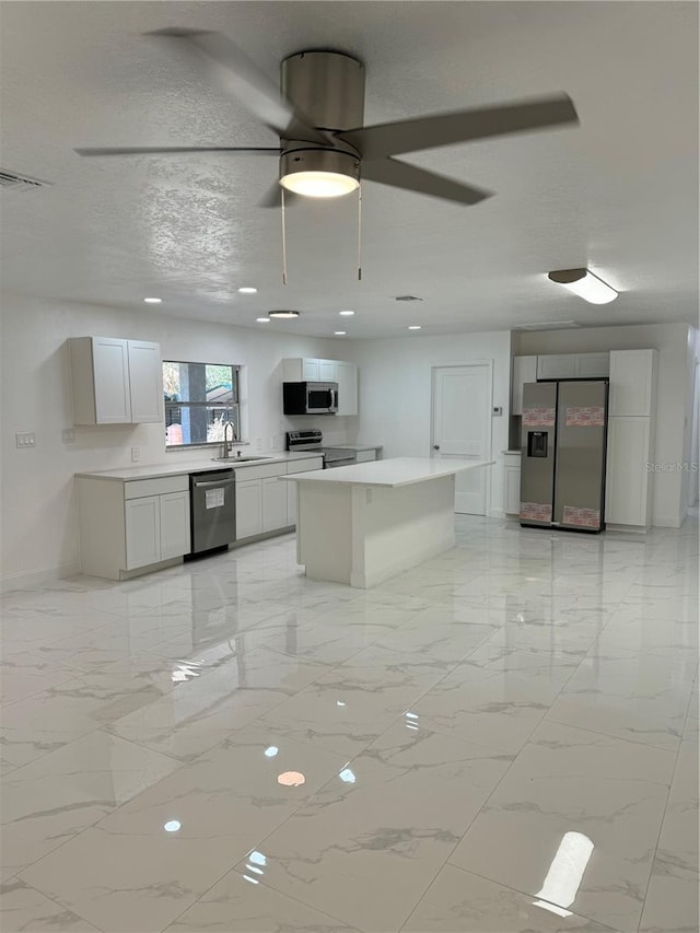 kitchen featuring ceiling fan, a center island, a textured ceiling, white cabinets, and appliances with stainless steel finishes