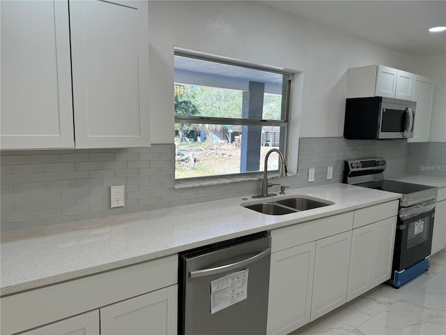 kitchen featuring tasteful backsplash, light stone counters, stainless steel appliances, sink, and white cabinetry