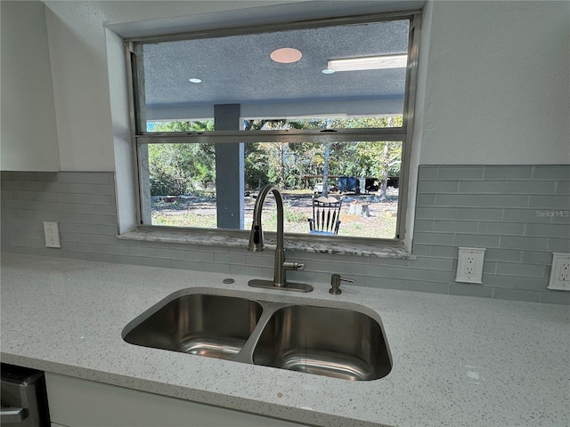 interior details featuring tasteful backsplash, light stone countertops, and sink