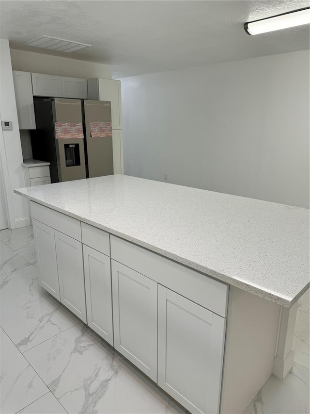 kitchen with stainless steel fridge, white cabinetry, and light stone counters