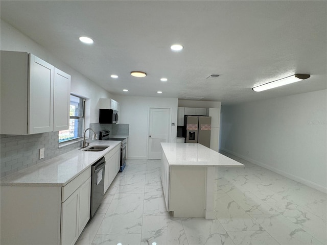 kitchen with sink, appliances with stainless steel finishes, a kitchen island, light stone counters, and white cabinetry