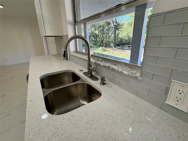 details featuring backsplash, light stone countertops, baseboards, and a sink