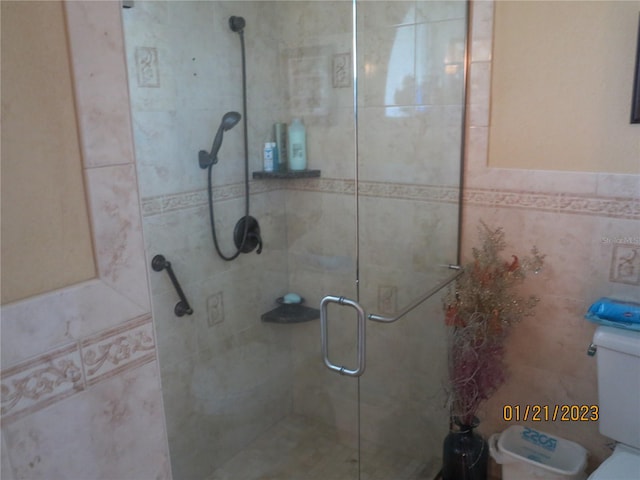 bathroom featuring toilet, an enclosed shower, and tile walls